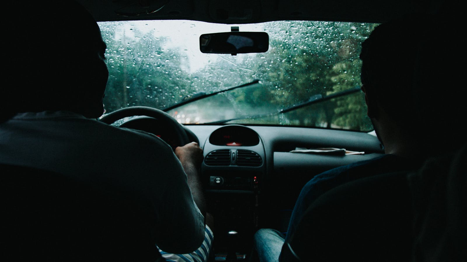 non standard auto Two people drive through rainy São Paulo streets, wet windshield and raindrops visible.